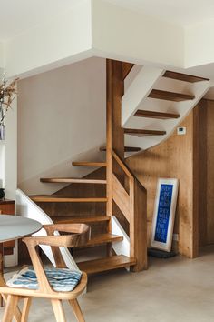 there is a wooden stair case next to the table and chair in this living room