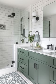 a bathroom with green cabinets and marble counter tops, along with a white tiled shower