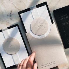 two black and white envelopes are being held by a woman's hand on a marble surface