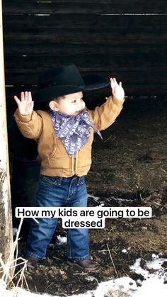 a little boy wearing a cowboy hat and scarf standing in the snow with his hands up