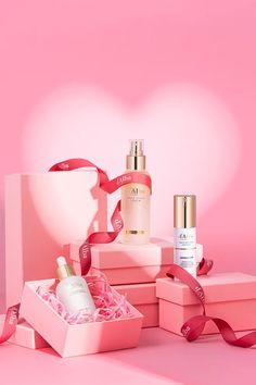 an assortment of skin care products in pink boxes with ribbon on the top and two bottles next to each other