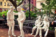 three white statues sitting on top of a park bench