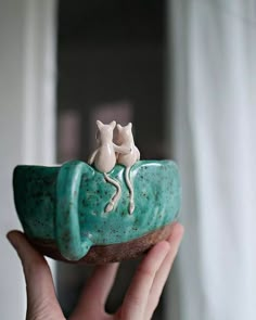 a person holding a small ceramic animal on top of a green object in their hand