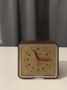 an alarm clock sitting on top of a white table next to a curtained window