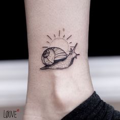 a small tattoo on the ankle of a woman's foot with a snail and sun