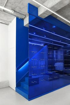 an empty room with blue glass walls and white flooring in the center is lit by fluorescent lighting