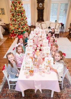 a group of children sitting at a table in front of a christmas tree with presents on it