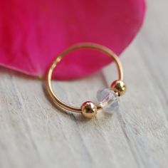 a close up of a gold ring on a wooden surface with a pink flower in the background