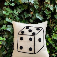 a white pillow with black dots on it sitting in front of some green plants and ivy