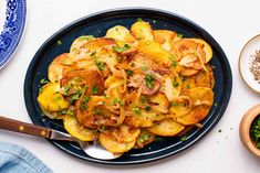 a blue plate topped with potatoes and onions next to two bowls of seasoning on a white table