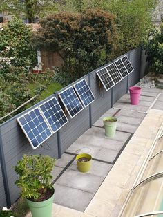 several solar panels on the side of a house next to potted plants and trees