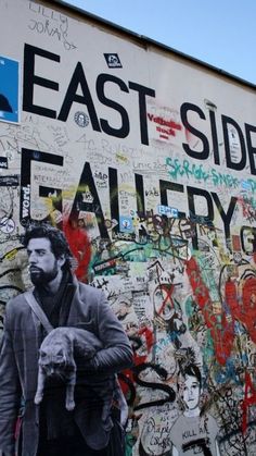 a man holding a cat next to a wall covered in graffiti