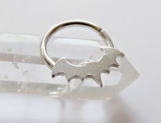 a silver bat ring sitting on top of a piece of clear glass with a white background