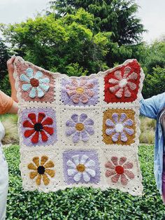 two women holding up a crocheted blanket with flowers on it