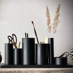 several black containers with scissors and other items in them on a table next to a vase