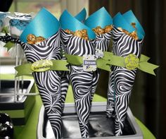 three zebra print party favors with blue hats and ribbons on display in a silver tray