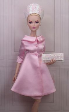 a barbie doll wearing a pink dress and hat with a white box in her hand