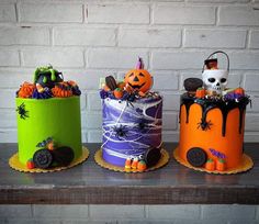 three decorated cakes sitting on top of a wooden table next to a brick wall with halloween decorations