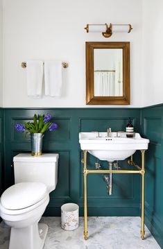 a white toilet sitting next to a sink in a bathroom under a mirror with gold trim