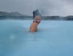 a woman is smiling in the middle of a blue lagoon with mountains in the background