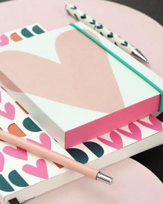 two notebooks with hearts on them sitting next to a pen and paper clipping