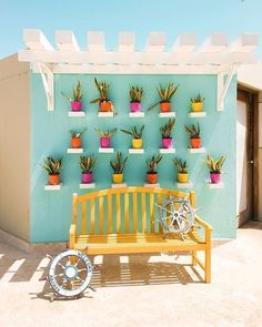 a yellow bench sitting in front of a blue wall with potted plants on it