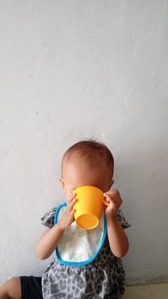 a baby sitting on the floor drinking from a yellow cup