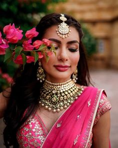 a woman wearing a pink sari and gold jewelry with flowers in her hair is posing for the camera