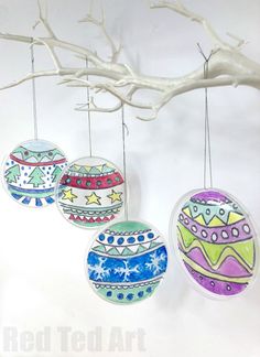 three ornaments hanging from a tree branch on a white wall with branches in the background