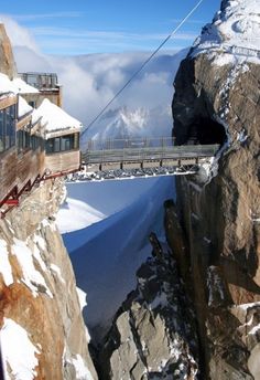 a cable car going over a snow covered mountain side with mountains in the background and clouds