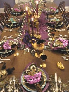 the table is set with purple and gold plates, silverware, and masquerade masks