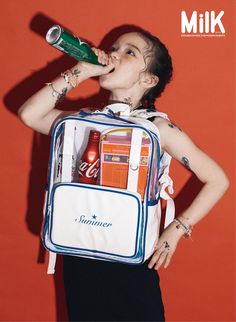 a young woman is drinking from a bottle while wearing a backpack with soda cans on it