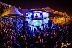 a large group of people standing around in front of a building with lights on it