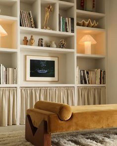 a living room filled with lots of white bookshelves next to a window covered in curtains