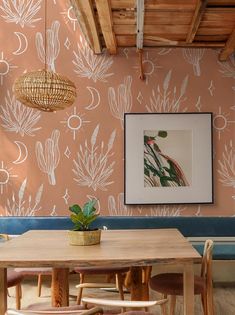 a dining room table and chairs in front of a pink wall with white drawings on it