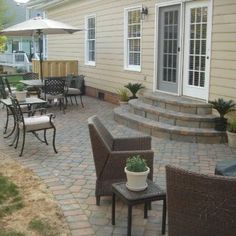 a patio with chairs, tables and an umbrella in the back yard next to a house