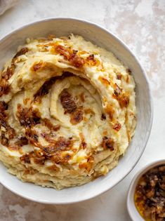 a white bowl filled with mashed potatoes next to two small bowls of sauces