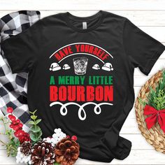 a merry little bourbon t - shirt on a table next to pine cones and christmas decorations