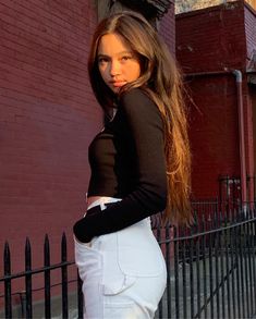 a woman standing in front of a fence with her hand on her hip and looking at the camera