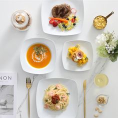 four square plates with different types of food on them next to a cookbook and utensils