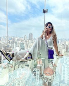 a woman in white pants and sunglasses is hanging off the side of a high rise building