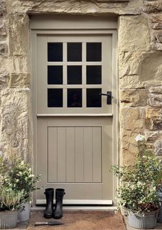 a pair of black rubber boots sitting in front of a stone building with two planters