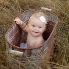 a baby sitting in a bucket on top of some tall grass and looking at the camera