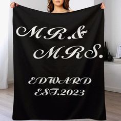 a woman holding up a black and white wedding blanket with the names mr and mrs printed on it