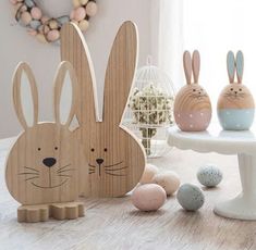 wooden easter decorations with bunny ears and eggs in front of them on a white table