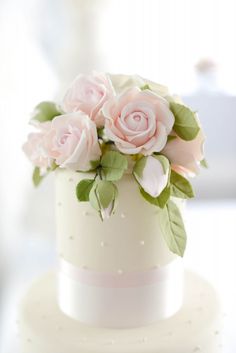 there is a white cake with pink flowers on the top and green leaves on the bottom