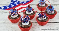 chocolate cupcakes decorated with red, white and blue sprinkles are sitting in front of an american flag