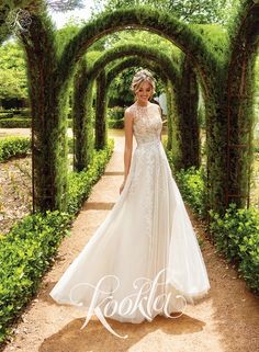 a woman in a wedding dress is walking through an archway with greenery on either side