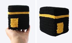 a hand holding up a crocheted black and yellow object with two sides that have stripes on each side