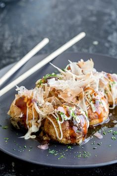 some food is on a black plate with chopsticks